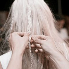 a woman is braiding her hair with a piece of white yarn in front of her face