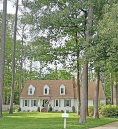 a white house surrounded by trees in the middle of a green yard with a sign