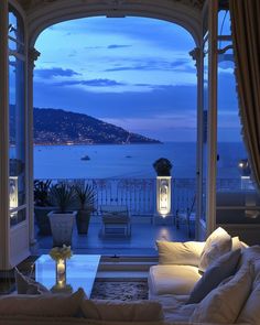 a living room filled with furniture and a large window overlooking the ocean at night time