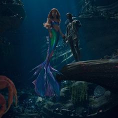 a mermaid standing next to a man in the ocean