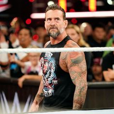 a man with tattoos standing in front of a wrestling ring