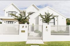 a white house with two trees in front of it and a fence around the yard