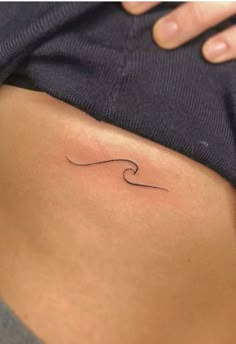 a woman's stomach with a small wave tattoo on her lower back side ribcage