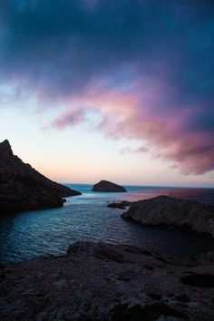 the sky is purple and blue as it sits over some rocky coastlines in the distance