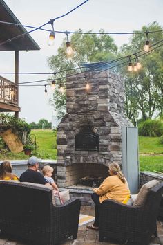 people sitting in wicker chairs around an outdoor fireplace with lights strung over the fire place