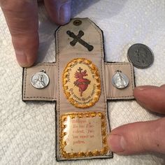 a cross made out of paper with some coins on the side and one hand holding it