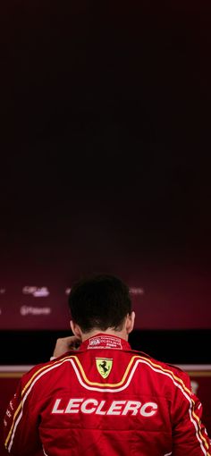 a man in a red racing suit sitting on top of a chair with his back to the camera