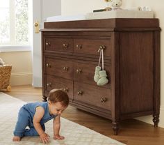 a baby crawling on the floor in front of a dresser