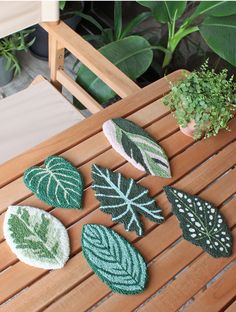 four green and white leaf shaped rugs sitting on top of a wooden table next to a potted plant