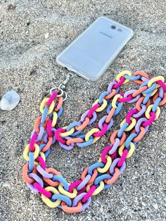 a cell phone laying on the ground next to a colorful chain necklace and earring