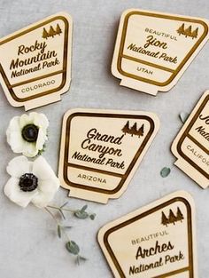 four wooden badges with white flowers in them on a gray surface next to some leaves