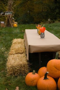 pumpkins and hay bales on the ground in front of a table with two vases