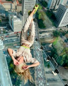 a woman hanging upside down in the air on top of a building with her feet up