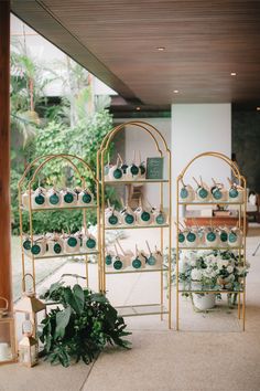 a display case filled with lots of cupcakes on top of metal racks next to plants