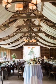 the inside of a wedding reception with white draping and lights hanging from the ceiling