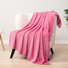 a pink blanket sitting on top of a white chair next to a potted plant