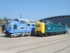 two trains are parked next to each other in front of a large blue and yellow building