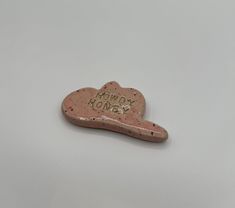 a pink heart shaped brooch with the words honey honey on it