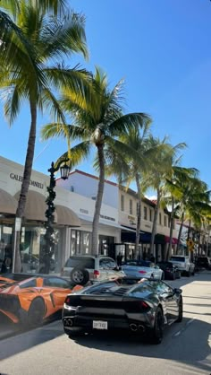 the cars are parked on the side of the road in front of the shops and palm trees