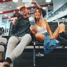 a man and woman sitting on a bench at an airport holding up tickets to their faces