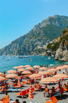 many people are sitting on the beach under umbrellas