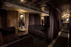 a living room with couches, mirrors and lights on the ceiling in front of a brick wall