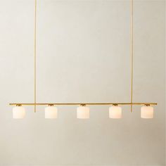 four lights hanging from a gold bar with white glass shades on the top and bottom