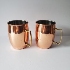 two shiny metal mugs sitting next to each other on a white surface with no one around them