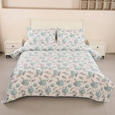 a white bed with blue flowers on it and two night stands in front of the bed