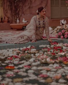 a woman sitting on the ground in front of flowers and water with petals all over it