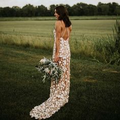 a woman is standing in the grass holding a bouquet and looking off into the distance