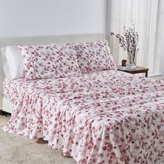 a white bed with red flowers on it in a room next to a large window