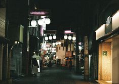 an empty street at night with people walking on the sidewalk and lights hanging from buildings