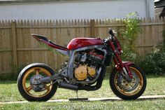 a red and black motorcycle parked on top of a grass covered field next to a fence