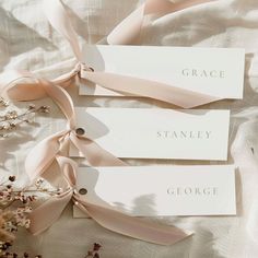 three place cards with ribbons tied around them on a bed sheet, some flowers in the foreground