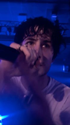 a man holding a microphone up to his face in front of a blue lit room