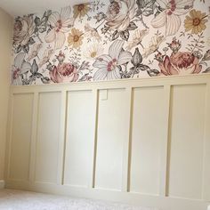 an empty room with white paneling and floral wallpaper on the walls, in front of a window