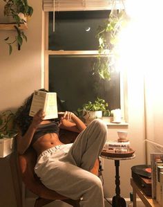 a woman reading a book while sitting in a chair next to a window at night