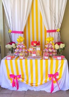 candy bar with yellow and white striped table cloth, pink bow ties, flowers and candies