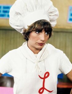 a woman wearing a chef's hat with the letter j on it, standing in front of a counter