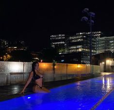 a woman sitting on the edge of a swimming pool at night