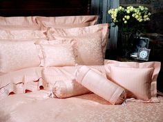 a bed with pink comforters and pillows on top of it next to a vase filled with flowers