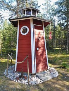 a small red and white building in the middle of a forest with rocks around it