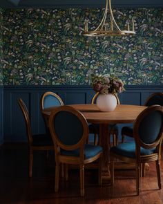 a dining room table with blue chairs and wallpaper