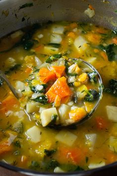 a ladle full of soup with carrots, spinach and other veggies