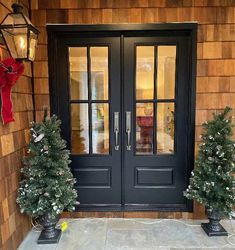 two potted christmas trees sitting in front of a black double door