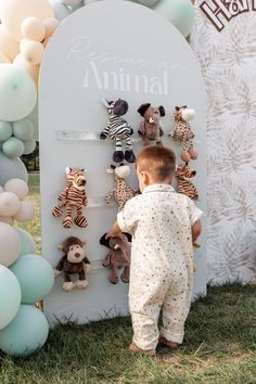 a little boy standing in front of a sign with stuffed animals on it's side