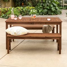 a wooden table with two benches in front of some plants and flowers on the ground