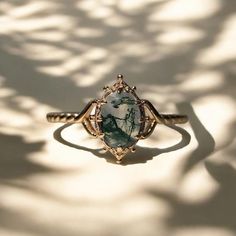 a ring with a green stone in the center on a white background that is casting a shadow