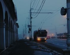 a bus is driving down the street in the rain at night with its headlights on